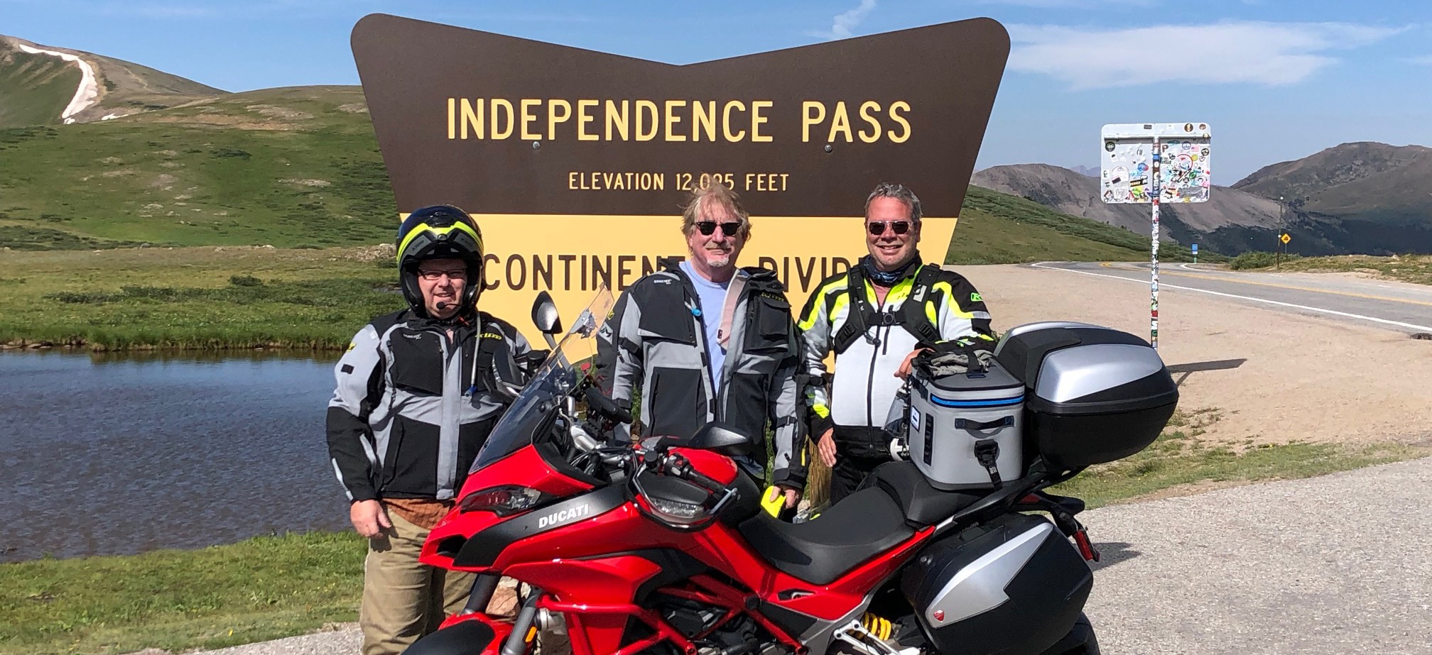 Three motorcycles and their drivers in front of sign on Independence Pass near Aspen, Colorado.